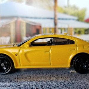 May include: A yellow Dodge Charger diecast car model with black wheels. The car has a black interior and a black spoiler.