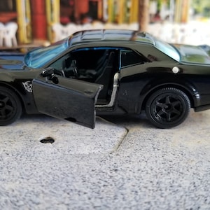 May include: A black toy car with a door open, the car is a Dodge Challenger.