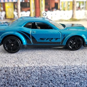 May include: A blue Dodge Challenger SRT diecast car with black accents and wheels. The car is a replica of a real car and is a popular collectible.
