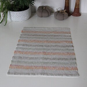 May include: A woven placemat with a striped pattern in shades of beige, gray, and orange. The placemat is on a white table.