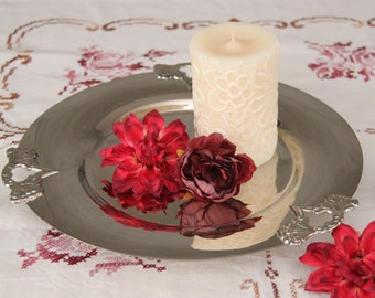Può includere: Un vassoio d'argento con una candela bianca e fiori rossi e bordeaux. Il vassoio ha due manici decorati.