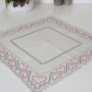 May include: White tablecloth with a grey and pink embroidered heart border.