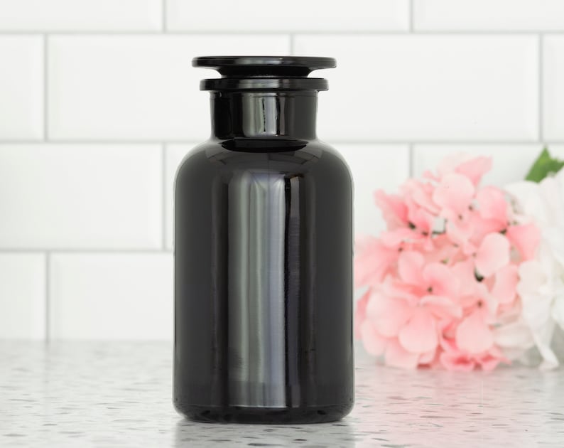 May include: A black glass bottle with a black lid. The bottle is opaque and has a smooth, shiny finish. It is sitting on a white countertop.