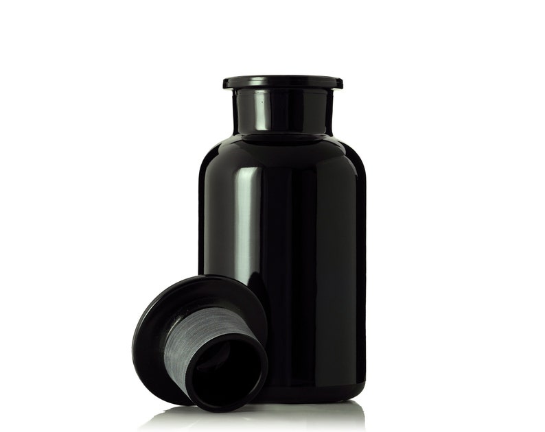May include: A black glass bottle with a black lid. The lid is off and sitting next to the bottle.
