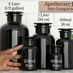 May include: A size comparison of five black glass apothecary jars with black lids. The jars are labeled with their volume in milliliters and ounces: 2 liters (1/2 gallon), 1 liter (34 oz), 500 ml (16 oz), 250 ml (8 oz), and 100 ml (4 oz).
