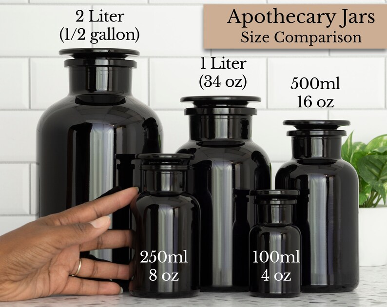 May include: A size comparison of five black glass apothecary jars with black lids. The jars are labeled with their volume in milliliters and ounces: 2 liters (1/2 gallon), 1 liter (34 oz), 500 ml (16 oz), 250 ml (8 oz), and 100 ml (4 oz).