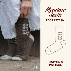 Könnte beinhalten: Braune Strickstrümpfe mit hellgrauer Spitze und Ferse sowie einem weißen Blumenmotiv am Knöchel. Das Bild enthält den Text Meadow Socks PDF PATTERN und KNITTING PATTERN sowie eine Strichzeichnung des Sockenentwurfs mit einer Blume.