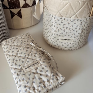 Puede incluir: Una colecci&oacute;n de cestas de almacenamiento y un estuche de tela acolchada. Las cestas y el estuche son de color crema con un estampado floral azul. El estuche est&aacute; atado con una cinta color crema. El texto "morgenstund making" es visible.