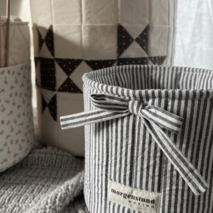 Puede incluir: Tres cestas de almacenamiento de tela en varios tama&ntilde;os y patrones. La cesta delantera tiene rayas verticales en blanco y negro con un lazo y una etiqueta que dice "morgenstund making". La cesta del medio tiene un dise&ntilde;o de patchwork. La tercera cesta tiene un estampado floral.