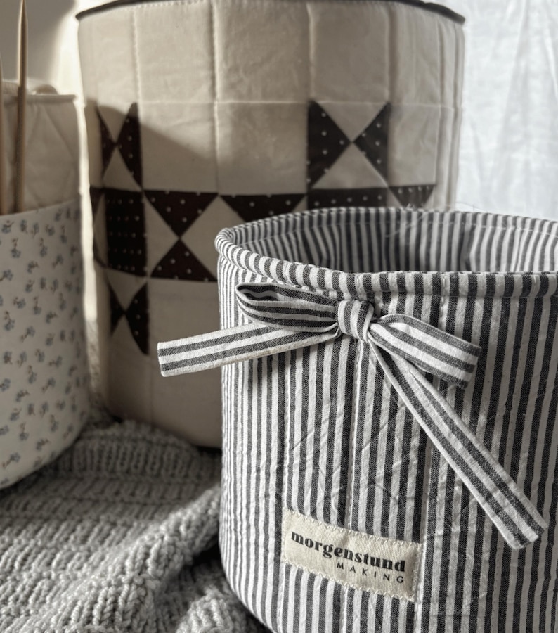 Puede incluir: Tres cestas de almacenamiento de tela en varios tama&ntilde;os y patrones. La cesta delantera tiene rayas verticales en blanco y negro con un lazo y una etiqueta que dice "morgenstund making". La cesta del medio tiene un dise&ntilde;o de patchwork. La tercera cesta tiene un estampado floral.