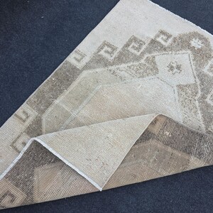 May include: Beige and brown vintage rug with geometric patterns. The rug features a central design with a repeating square motif and a border with a similar pattern. The rug is folded over, revealing the underside.