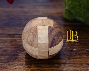 Peut inclure: Une boule de puzzle en bois avec un motif de grain de bois brun clair et brun foncé. La boule est composée de pièces qui s'emboîtent et peuvent être réarrangées.