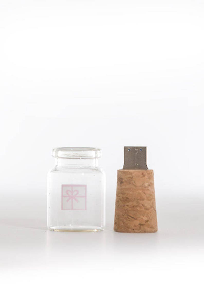 Peut inclure: Une bouteille en verre transparente avec un bouchon en li&egrave;ge, orn&eacute;e d'un cadeau rose avec un n&oelig;ud sur le devant. La bouteille est vide et le bouchon est de couleur brun naturel.
