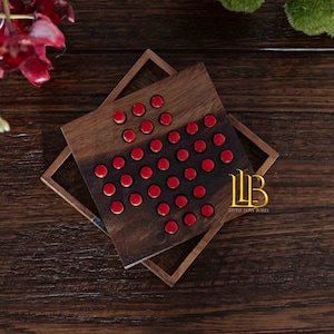 May include: A wooden game board with a heart-shaped pattern of red pegs. The board is made of dark wood and has a light brown border. The text "Little Love Boxes" is printed on the board.