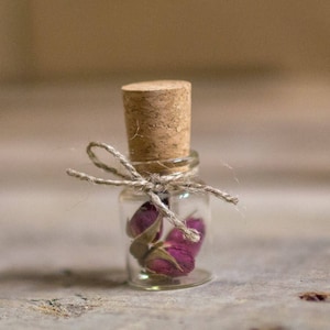 Peut inclure: Une petite bouteille en verre avec un bouchon en li&egrave;ge, attach&eacute;e avec de la ficelle, contenant des boutons de roses roses s&eacute;ch&eacute;s.