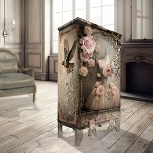 May include: A vintage-style cabinet with a distressed white finish. The cabinet is decorated with a floral design featuring pink roses, a bird, and a gold-leaf accent. The cabinet has a single drawer and two doors.