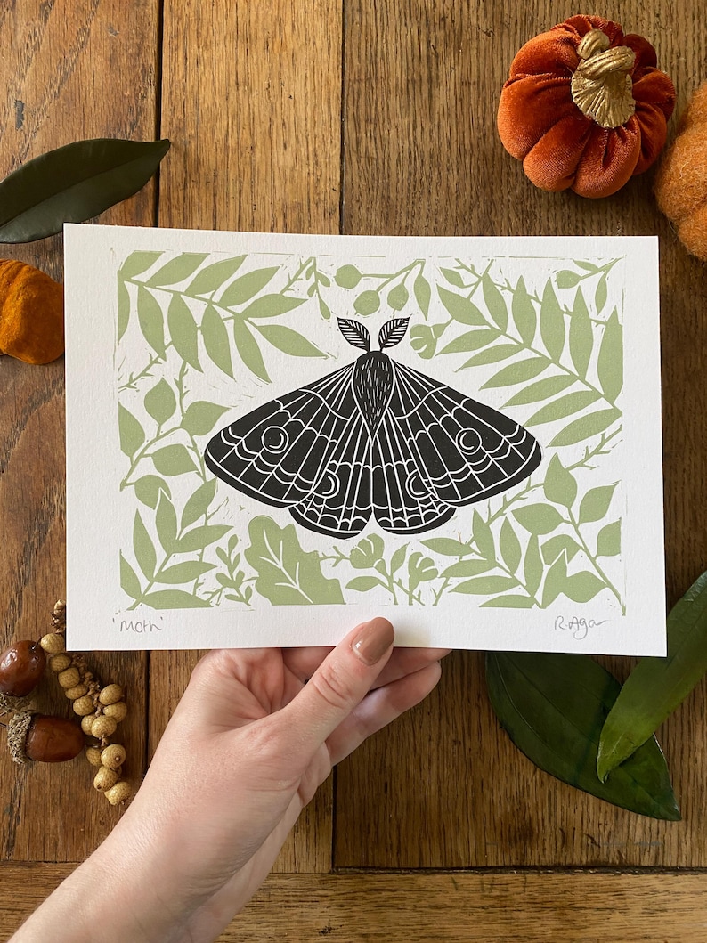 May include: A black and white moth print with a light green leaf pattern background. The word "Moth" is printed at the bottom left corner. The print is on white paper.