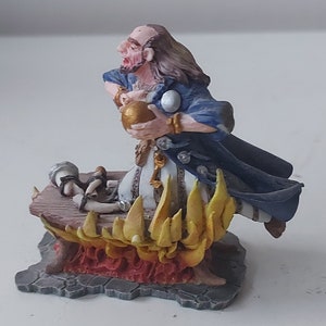 May include: A blue and white painted figurine of a wizard holding a golden orb, standing on a base with flames. The wizard is wearing a blue robe and has a long white beard.