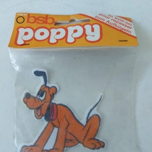 Op de afbeelding: Een bruine en witte cartoon hond strijk-op patch met de tekst "to iron-on pour repasser zum Aufbügeln" op de verpakking.