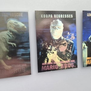 May include: Three Super Mario Bros. trading cards. The first card features a dinosaur with the text "IN THE RESCUE". The second card shows a figure wrapped in bandages with the text "KOOPA REGRESSES". The third card displays a character with the text "LEMMY GOES GOOMBA!"