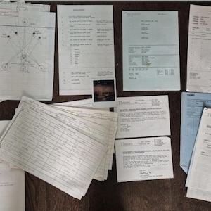 Könnte beinhalten: Eine Sammlung von Vintage-Dokumenten, darunter Diagramme, Listen und Rechnungen, die auf einer dunklen Holzoberfläche angeordnet sind. Einige Papiere haben handschriftliche Notizen und ein kleines Foto.