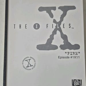 Puede incluir: Guion de rodaje blanco para el episodio "Fire" de "Expediente X", con el logotipo del programa y los detalles del episodio. El guion está encuadernado con una encuadernación negra y presenta el logotipo de 20th Century Fox.