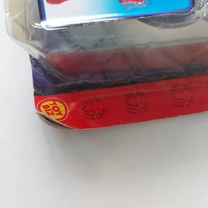 Pode incluir: Close-up de um logotipo Toy Biz vermelho e amarelo em um fundo vermelho com tr&ecirc;s desenhos de teia de aranha preta.