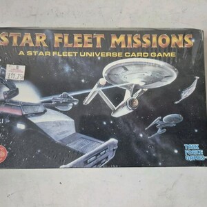 May include: A Star Fleet Missions card game box featuring a spaceship in space. The box is black with gold lettering and a red and white sticker. The game is a Task Force Games product.