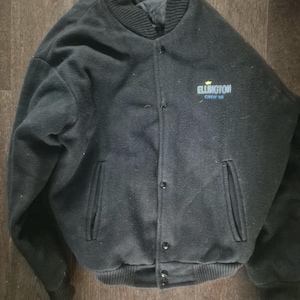 May include: Black varsity jacket with a ribbed collar, cuffs, and hem. The jacket has a button-up front, two front pockets, and the text "Ellington Crew 95" in blue and gold lettering on the chest. The jacket is made of a thick, wool-like material.
