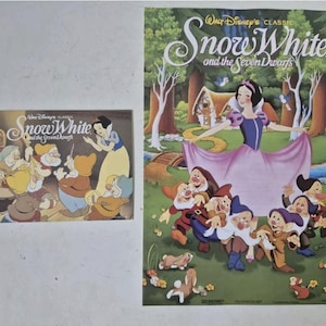 May include: Two images of Snow White and the Seven Dwarfs. The first image is a smaller card with a cartoon illustration of Snow White and the Seven Dwarfs. The second image is a larger poster with a cartoon illustration of Snow White and the Seven Dwarfs. The poster has the text "Walt Disney's Classic Snow White and the Seven Dwarfs".