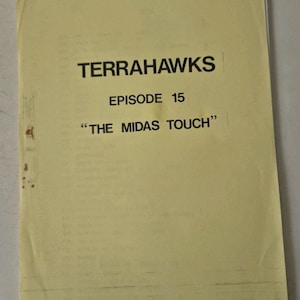 Puede incluir: Un guion amarillento con el título "TERRAHAWKS" en negrita negra. También muestra "EPISODIO 15" y el título del episodio "THE MIDAS TOUCH" entre comillas. El papel muestra signos de desgaste y envejecimiento.
