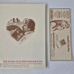 May include: A 1971 Royal Film Performance programme and ticket stub. The cream-coloured programme features a heart-shaped sepia photograph of Ali MacGraw and Ryan O'Neal, with text detailing the event at Odeon Theatre. The ticket stub includes matching details.