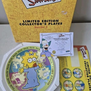 May include: A yellow and white box with the text "The Simpsons Limited Edition Collector's Plates Series 1" on the front. The box contains a ceramic plate with a cartoon image of Maggie Simpson, the baby from the Simpsons, with the text "Suck. Suck. Maggie Simpson" around the edge of the plate.