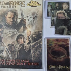 Puede incluir: Una hoja promocional de Topps Chrome de la trilogía El Señor de los Anillos con personajes de la película, junto a varias tarjetas coleccionables en fundas protectoras, incluyendo una de Gollum y otra del Anillo Único.