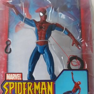 K&ouml;nnte beinhalten: Eine rote und blaue Spider-Man-Actionfigur mit einer Spinnwebenlinie, die an einem Reifen befestigt ist. Die Figur ist in einer Spinnweben-Schwing-Actionpose dargestellt. Die Verpackung zeigt das Marvel-Logo und den Text "Spider-Man Web-Line Spider-Man".