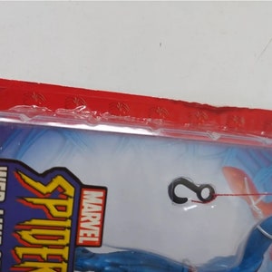 K&ouml;nnte beinhalten: Eine blaue und rote Marvel Spider-Man Actionfigur mit einer Web-Line-Funktion. Die Figur ist in einer durchsichtigen Plastik-Blisterverpackung mit einer roten Kopfkarte verpackt, auf der "MARVEL" und "WEB-LINE SPIDER-MAN" mit dem Text "with Web Climbing Action" steht.