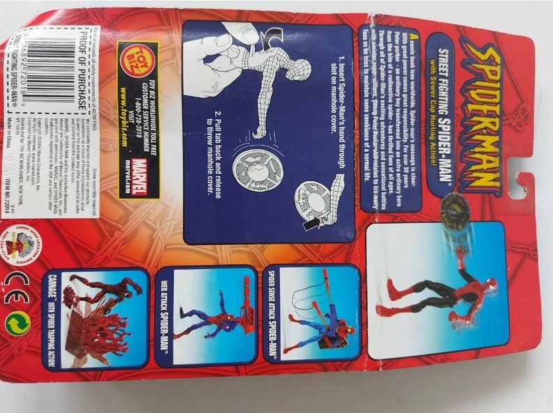 Pode incluir: Uma figura de a&ccedil;&atilde;o vermelha e preta do Homem-Aranha com uma tampa de esgoto na m&atilde;o. A figura &eacute; embalada em uma caixa de papel&atilde;o vermelha e azul com as palavras "Street Fighting Spider-Man" e "Sewer Cap Hurling Action!" impressas nela. A parte de tr&aacute;s da caixa mostra diferentes poses de a&ccedil;&atilde;o da figura.