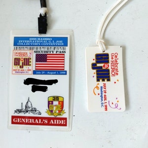 Könnte beinhalten: Zwei Vintage G.I. Joe Convention-Ausweise. Einer ist ein durchsichtiger Sicherheitsausweis mit der amerikanischen Flagge, dem Text "GENERAL'S AIDE" und den Daten 29. Juli bis 1. August 1999. Der andere ist ein weißes Etikett mit dem G.I. Joe-Logo.