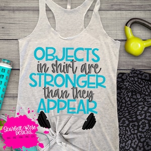May include: A gray tank top with the text "OBJECTS in shirt are STRONGER than they APPEAR" in blue and gray lettering.  Two blue dumbbells are below the text.