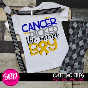 May include: A white t-shirt with the text "CANCER PICKED the wrong BOY" in blue, gray, and yellow lettering. A yellow ribbon is included in the design. The shirt is on a wooden surface with a pair of black and white suspenders and gray and white checkered pants.