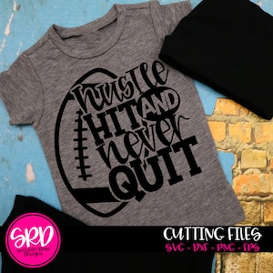 May include: A gray t-shirt with a black graphic of a football with the text "hustle hit and never quit".