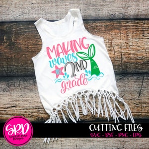 May include: A white tank top with a mermaid tail design and the text "Making waves in 2nd grade" in pink, blue, and green. The tank top has a fringe trim.
