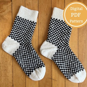 May include: A pair of black and white knit socks with a checkered pattern. The socks are laid out on a wooden surface. The text "Digital PDF Pattern" is visible in the upper right corner of the image.