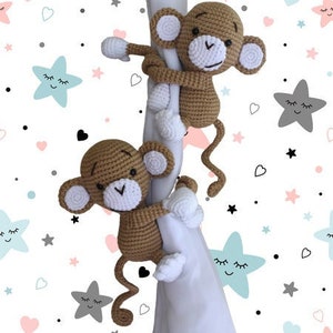May include: Two brown crocheted monkey toys with white faces and white arms and legs are climbing a white fabric. The fabric has a pattern of stars and hearts.