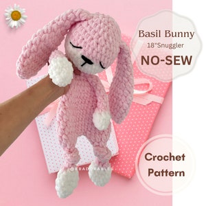 May include: Pink crocheted bunny plush toy with white accents. The bunny is 18 inches long and is a no-sew crochet pattern. The text "Basil Bunny 18" Snuggler NO-SEW Crochet Pattern" is visible in the image.