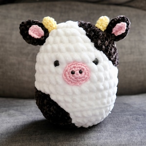 May include: A crocheted stuffed cow toy with black and white spots, yellow ears, and a pink nose.