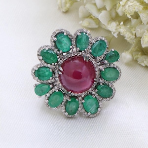 May include: A ring featuring a large red gemstone surrounded by smaller green gemstones and diamonds.