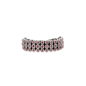 May include: A silver bracelet with three rows of red gemstones set in silver. The bracelet is made of a black cord.