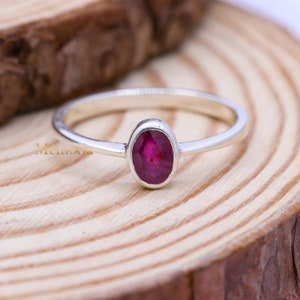 May include: A silver ring with a deep red oval gemstone. The ring is on a wooden surface.
