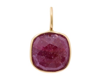 Puede incluir: Un colgante de oro con una piedra preciosa de rubí facetada. El rubí es de color rojo intenso y está engastado en un bisel de oro.
